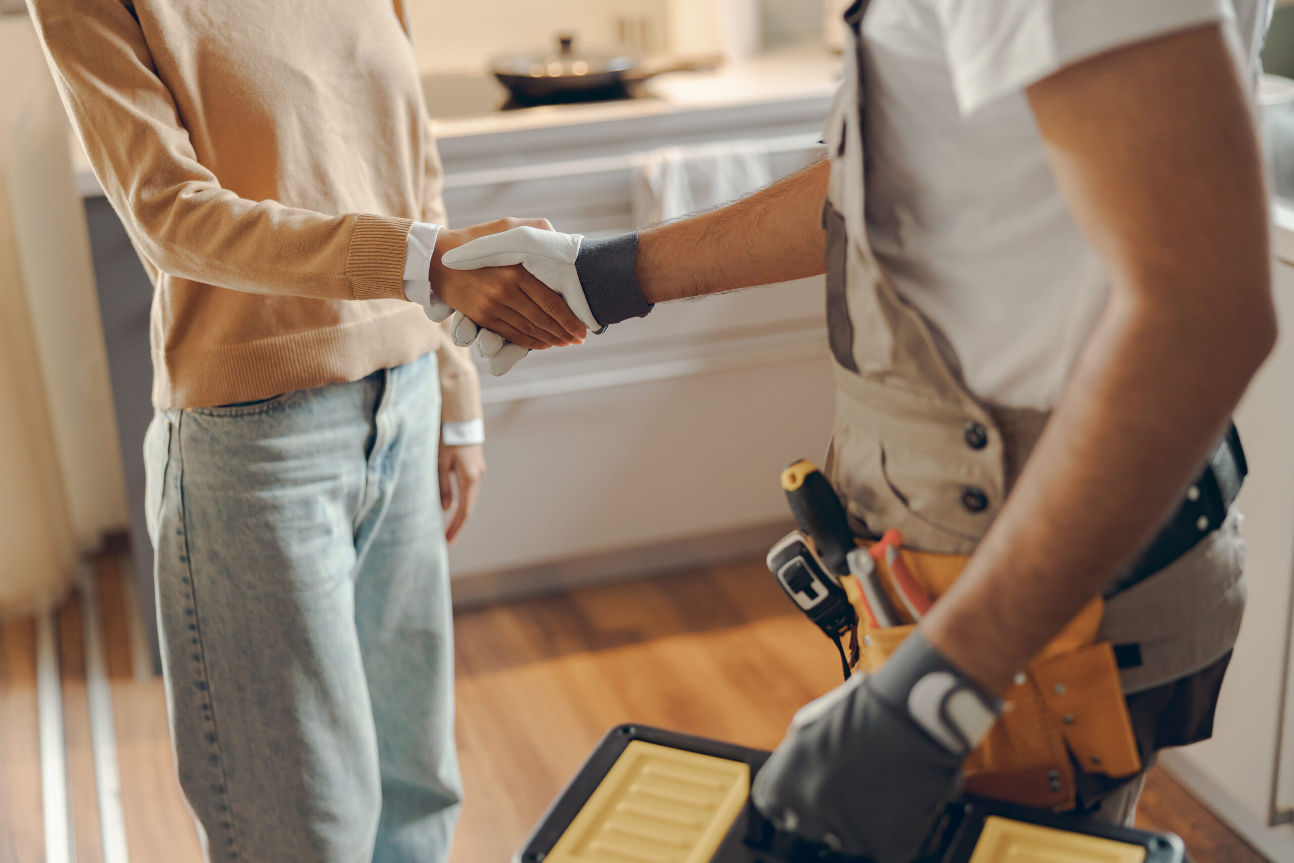 Technician wearing tool belt shaking hands with homeowner after successful home repair